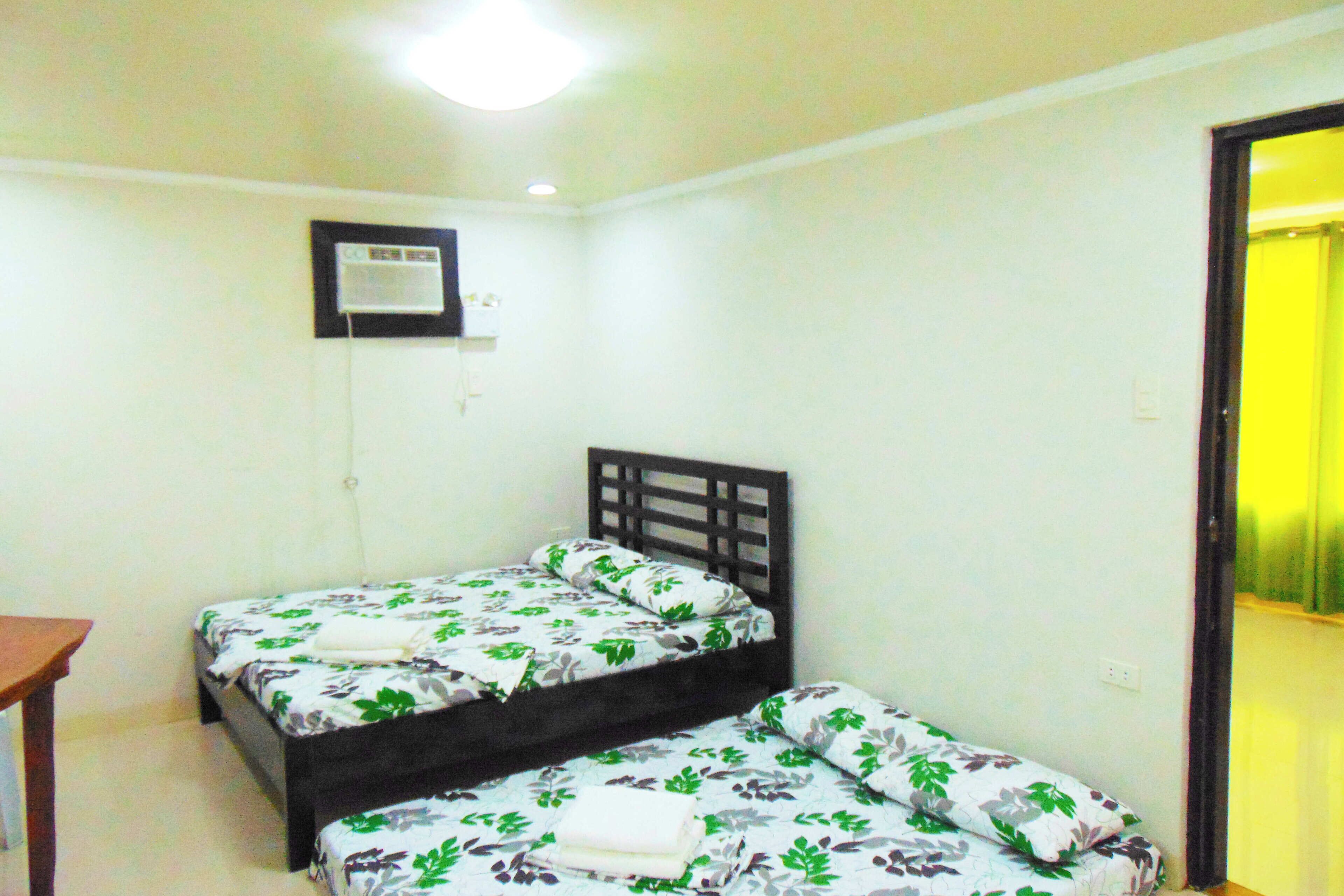 A room with two beds, a small table, and a wall-mounted air conditioner.