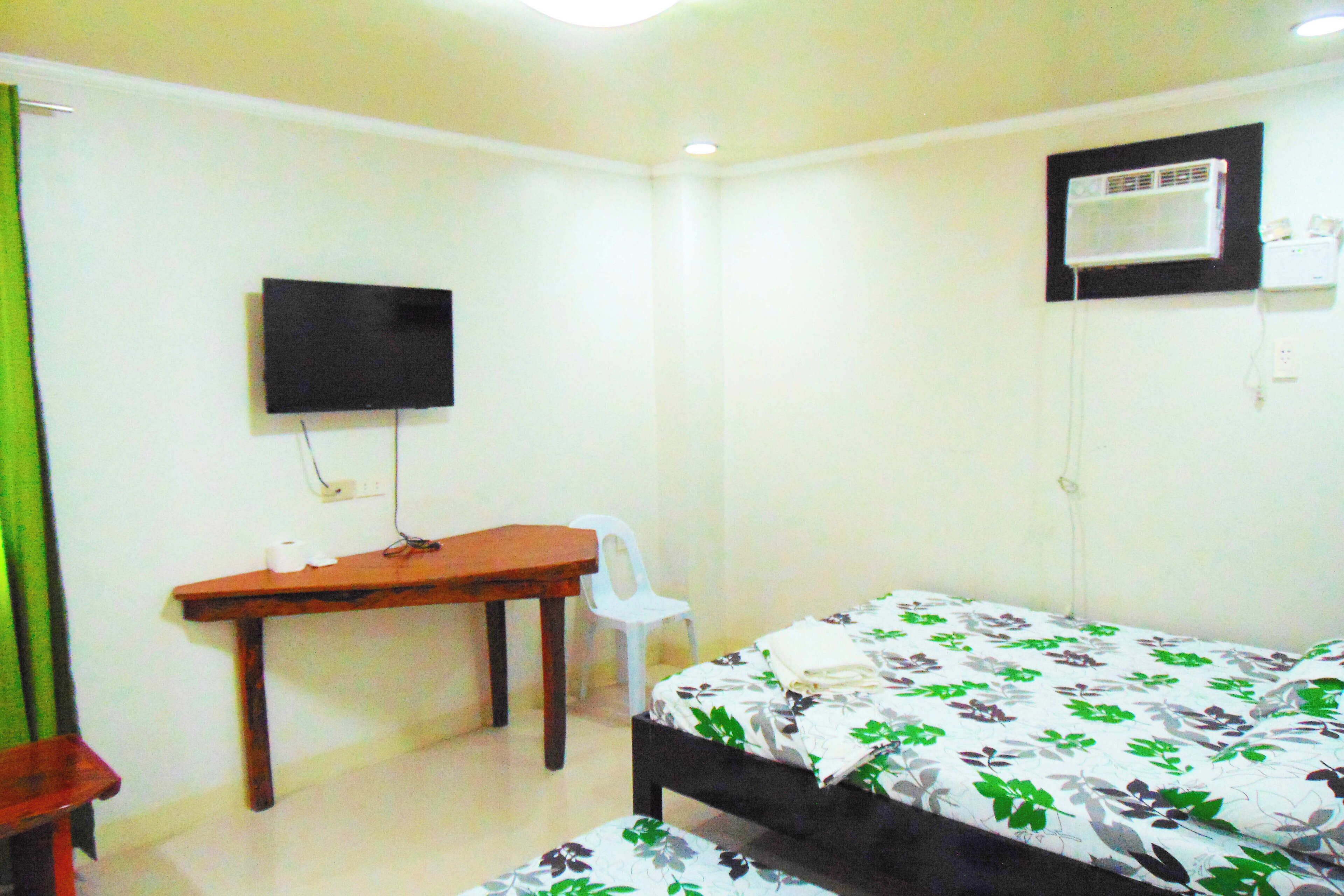 A small, clean room with a bed, a desk, a chair, and a television mounted on the wall.