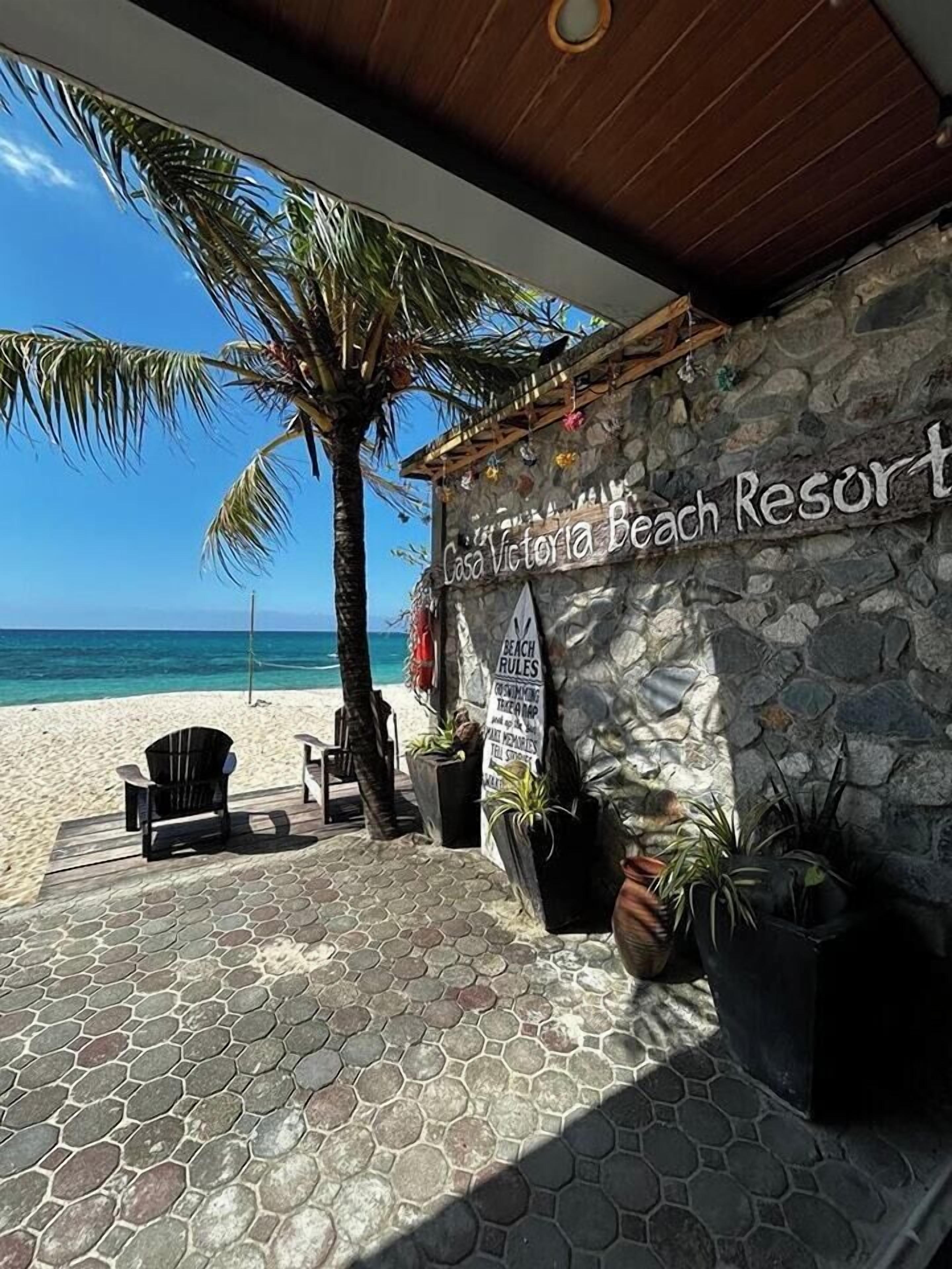 A beach resort named Casa Victoria Beach Resort with a stone wall, outdoor seating, and a view of the ocean.