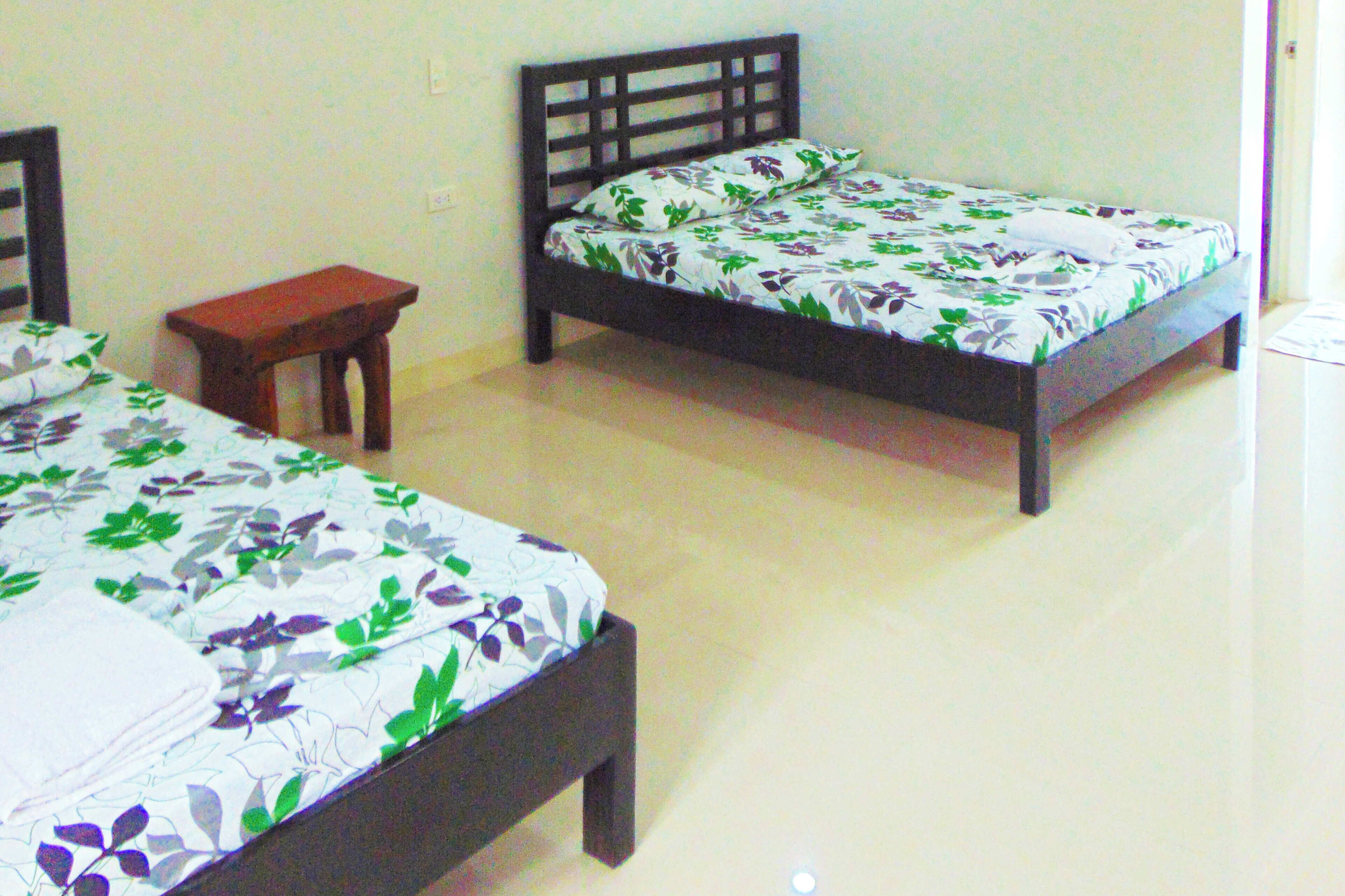 Two single beds with wooden frames and floral bedding, a small wooden table, and a plain wall.