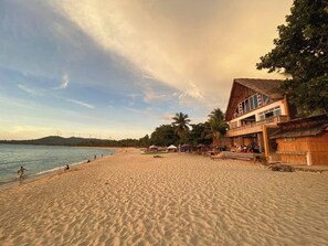 A beach with a building that has a thatched roof and a balcony. - Casa Victoria Beach Resort and Restaurant (Pagudpud)