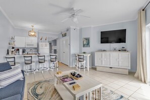 A modern living room with a sofa, coffee table, TV, and kitchen area with bar stools. - Tradewinds 1208 — Beach‑Front Escape with Sweeping 12th‑Floor Views (Orange Beach)