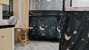 Un dormitorio con una cama cubierta por un dosel con temática espacial, una mesita de madera y un ventilador de techo.