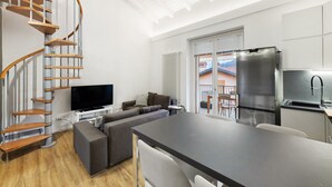 Un appartement moderne doté d’un escalier en colimaçon, d’un espace de vie avec un canapé et une télévision, d’une cuisine équipée d’un réfrigérateur et d’un coin repas.