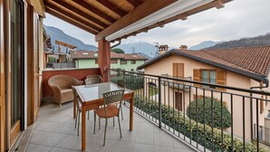 Un balcon doté d’un plafond en bois, une table avec des chaises et une vue sur les bâtiments et les montagnes environnants.