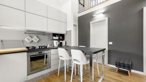 Une cuisine moderne avec des meubles blancs, un plan de travail noir et un petit coin repas avec des chaises blanches.