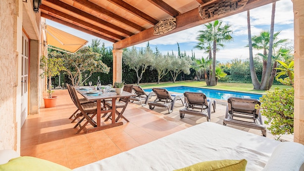 An outdoor patio with a pool, wooden pergola, and seating area.