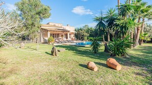 A house with a swimming pool, surrounded by palm trees and a well-maintained lawn.
