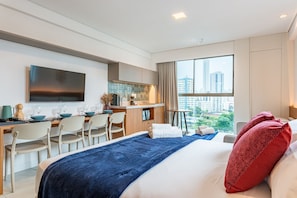 Quarto de hotel com cama, escrivaninha, televisão, vista da cidade e cozinha compacta.