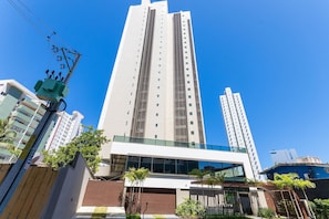 Um edifício moderno alto com fachada de vidro, vários andares e um céu azul claro.