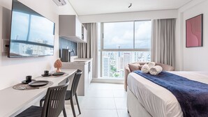 Une chambre d’hôtel moderne équipée d’un lit, d’un bureau avec une chaise, d’un téléviseur à écran plat, d’une fenêtre donnant sur la ville et d’un climatiseur fixé au mur.