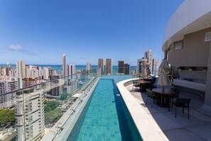 Piscina no terraço com vista para a cidade, área de estar externa e barreira de vidro.