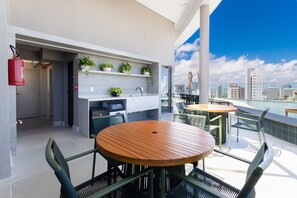 Une terrasse sur le toit avec une table et des chaises en bois, un petit coin cuisine agrémenté de plantes et une vue sur la ville.