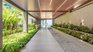 Un couloir au design moderne, avec un sol en béton, des panneaux de plafond en bois et une rangée de plantes de chaque côté.