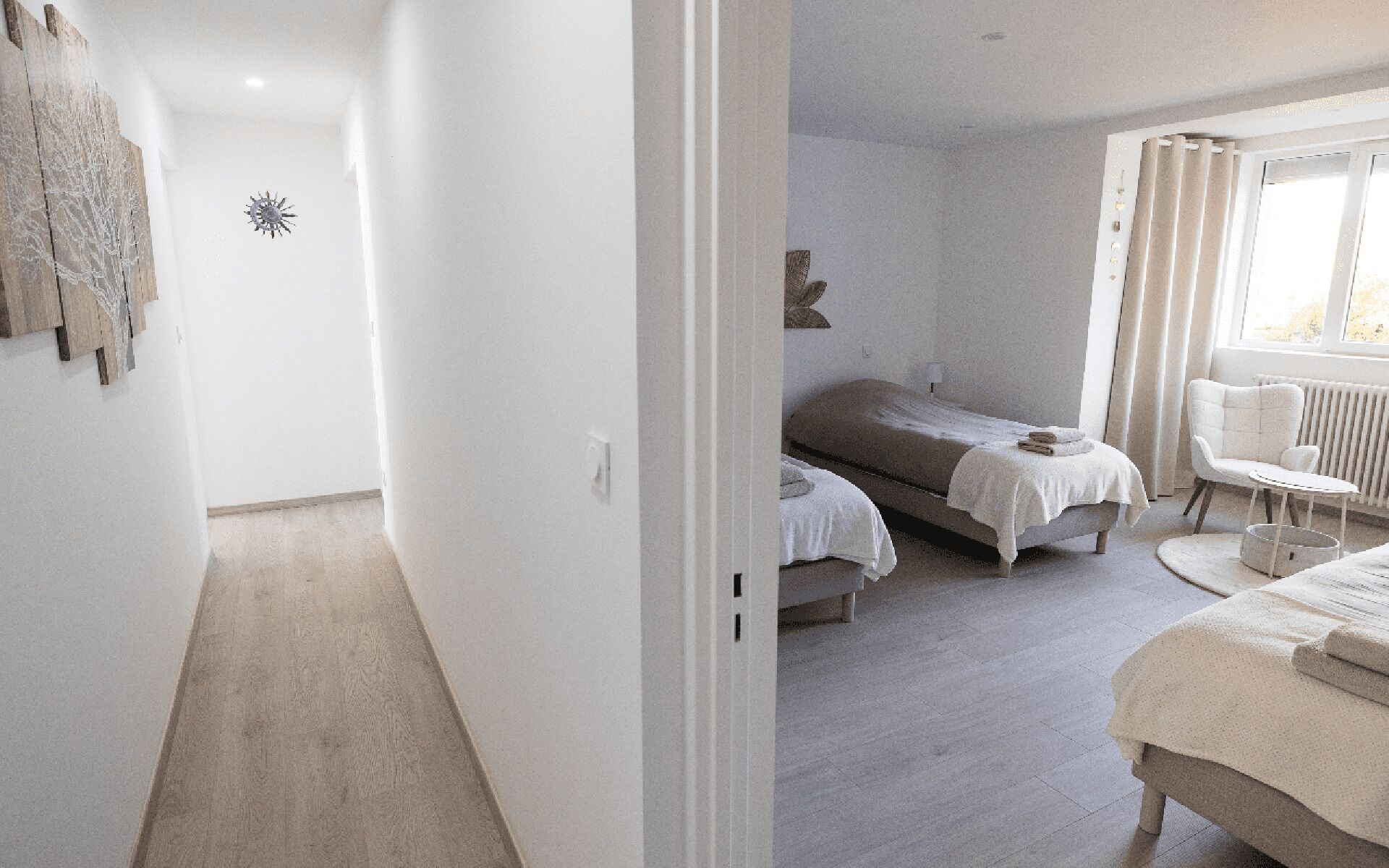 A bedroom with two beds, a window with curtains, a radiator, and a small table.