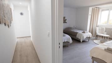 A bedroom with two beds, a window with curtains, a radiator, and a small table.