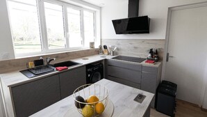 A modern kitchen with a large window, a built-in dishwasher, and a flat-screen TV mounted above the sink.