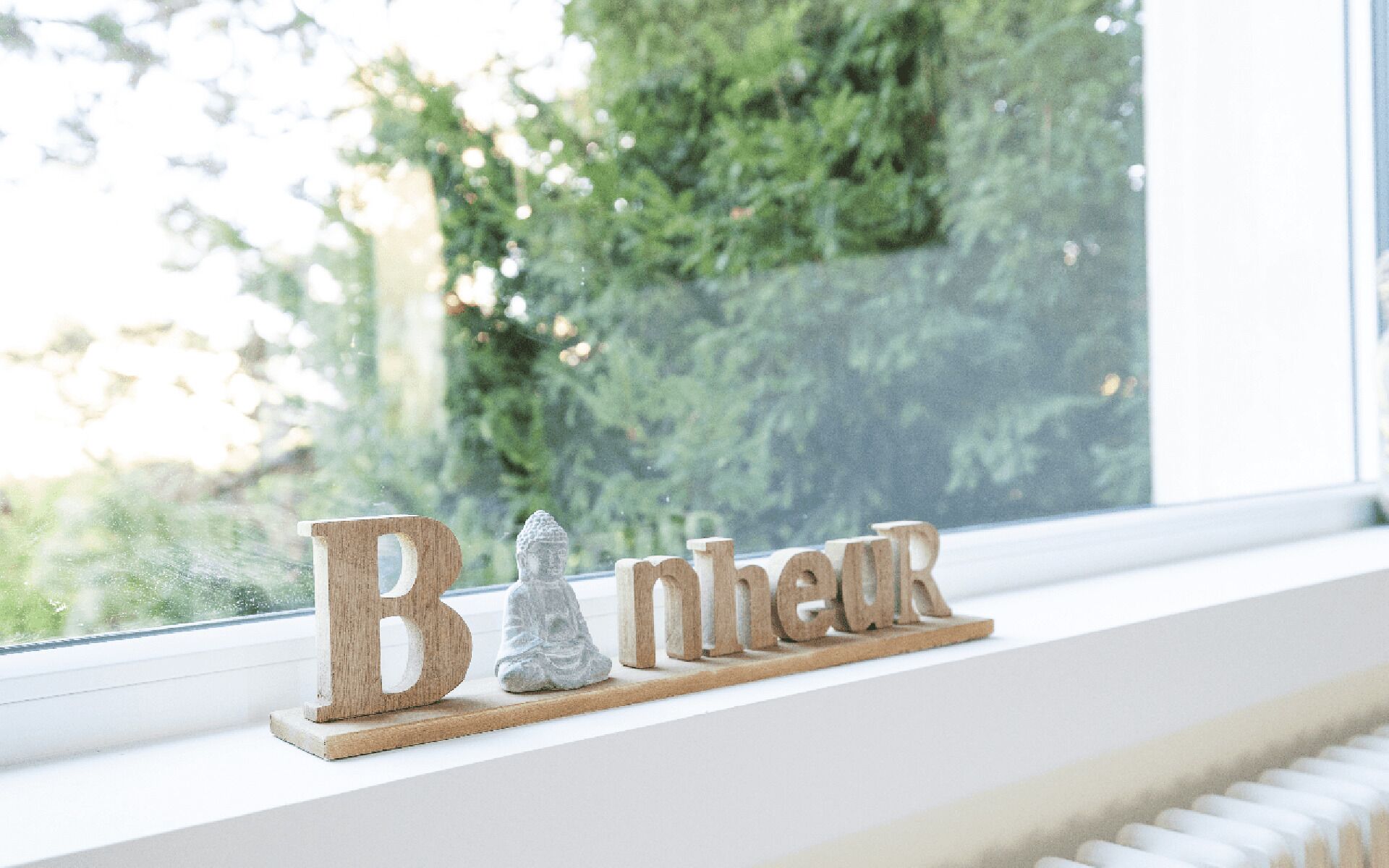 Un rebord de fenêtre orné de lettres en bois formant le mot « Bonjour » et d’une petite statue de Bouddha en pierre.