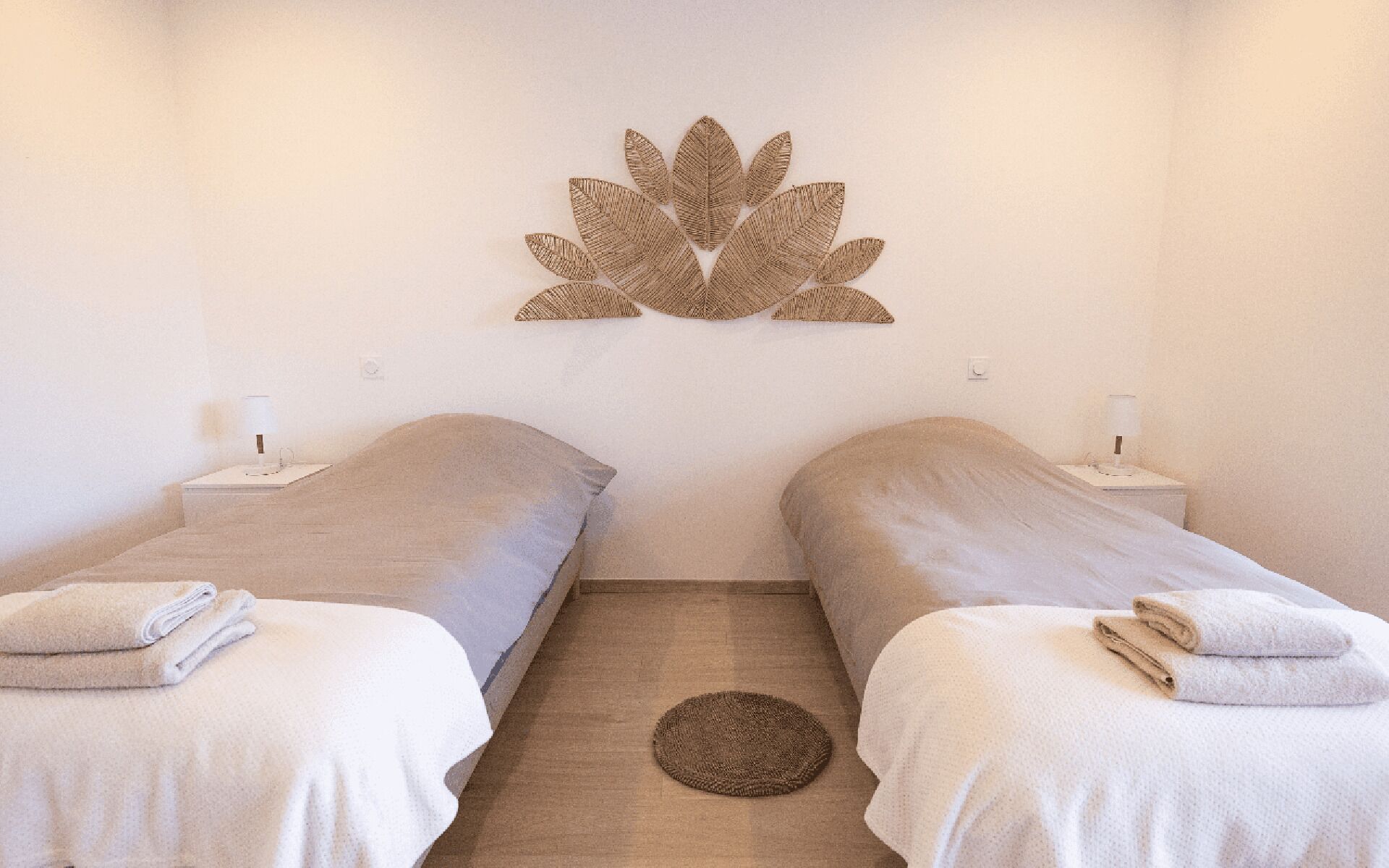 Une chambre avec deux lits simples, chacun étant équipé d’un oreiller et d’une serviette pliée. Un élément décoratif est fixé au mur au-dessus des lits.