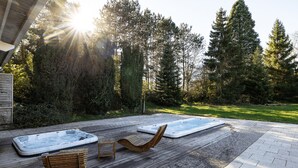 A wooden deck with two hot tubs and lounge chairs, surrounded by a forested area.