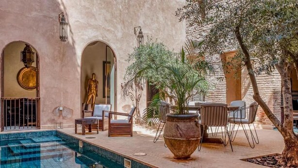 Zona de piscina con una estatua, mobiliario exterior y una maceta grande.