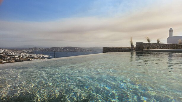 Una piscina cristalina con vistas a un pueblo costero y una torre al fondo.