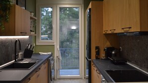 A modern kitchen with wooden cabinets, a black countertop, and a window overlooking a balcony.