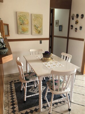 Ein Essbereich mit einem weißen Tisch, floralen Stühlen und einem gemusterten Teppich.