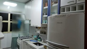 Une cuisine de taille réduite, avec des meubles blancs, une cuisinière, un évier et un réfrigérateur.
