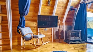 Una habitación acogedora con techo de madera, una mecedora, televisor y chimenea.