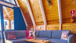 Una sala de estar acogedora con techo de madera, un sofá gris, una mesa de centro de madera y un tapete azul.