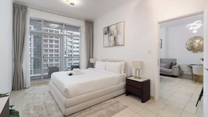 Une chambre moderne dotée d’un grand lit, d’une table de chevet, d’un bureau et offrant une vue sur la ville grâce à de grandes fenêtres du sol au plafond.
