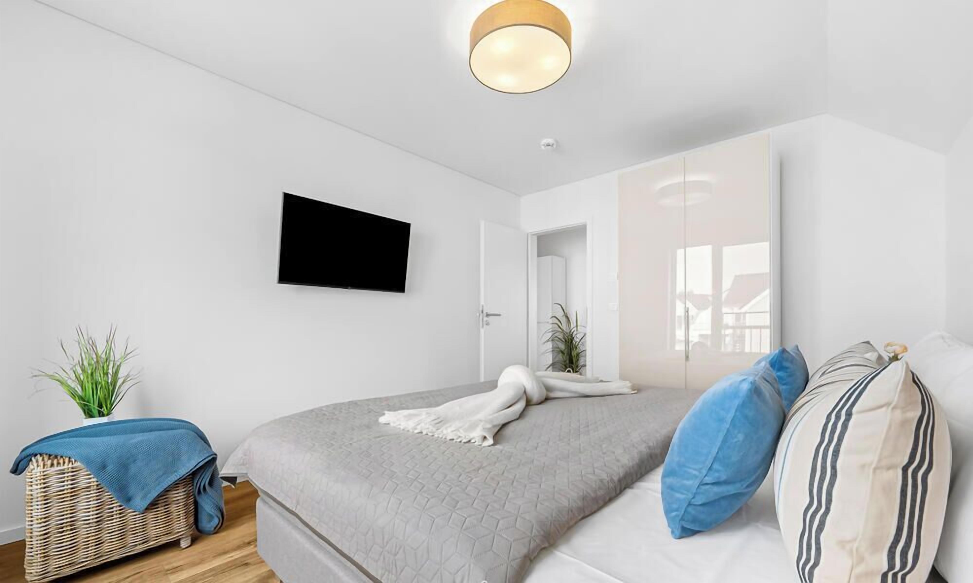 Une chambre à coucher moderne avec un lit, un téléviseur à écran plat, un panier en osier et une plante en pot.