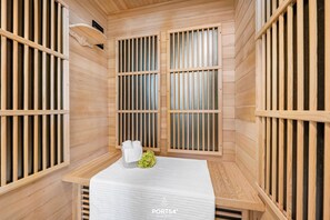 A sauna room with wooden walls and slatted windows, a bench, and a small table with towels and a decorative plant. - Schleiglück -Beach chair, infrared heat cabin, fireplace, balcony, parking space (Olpenitz)