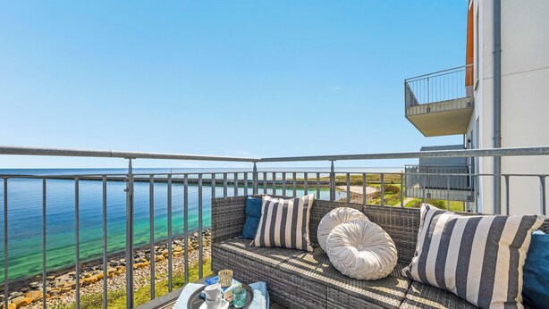 Un balcon avec vue sur la mer, des meubles en osier et un coin repas avec une table et des chaises.