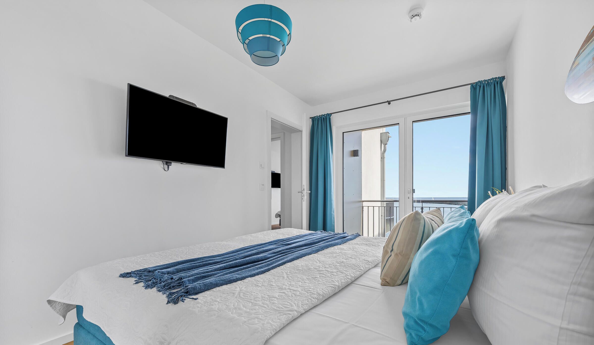 A modern bedroom with a bed, a TV, and a balcony with curtains.