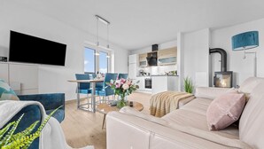 Ein modernes Wohnzimmer mit einer Couch, einem Flachbildfernseher, einem Essbereich mit Stühlen und einer Küche mit Herd.