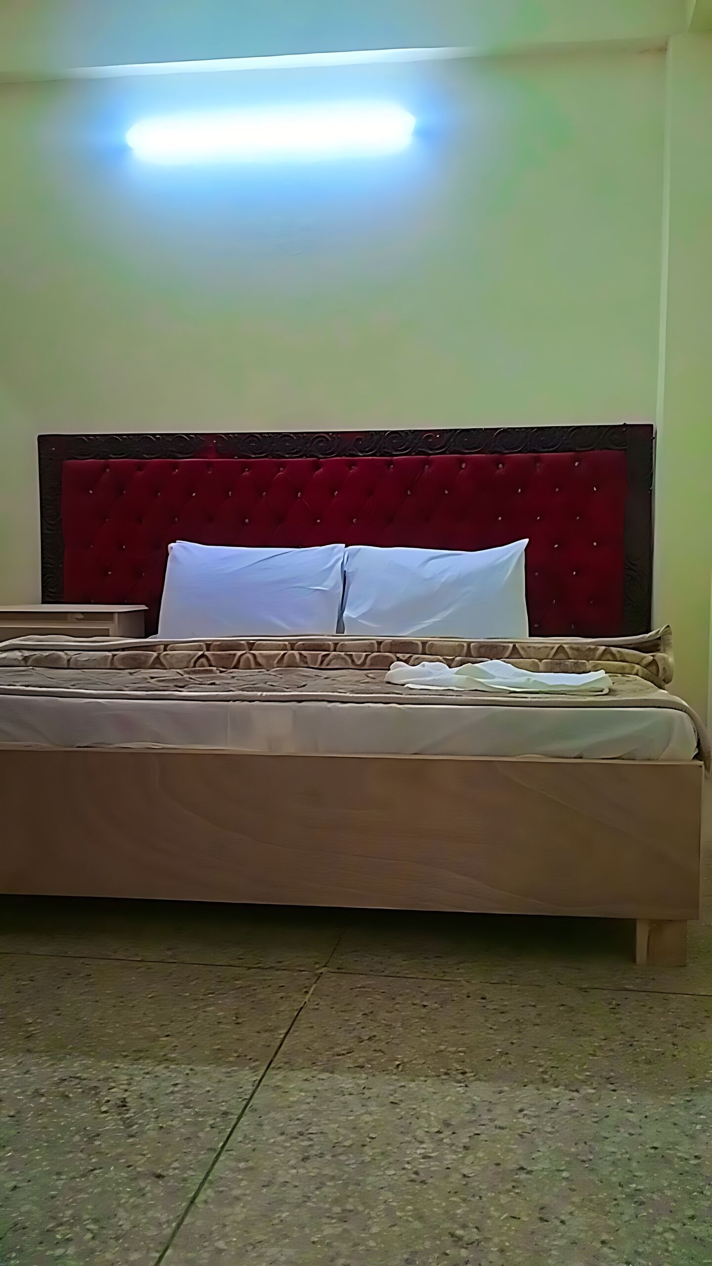 A room with a bed, a red headboard, and a ceiling light.
