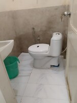 Une petite salle de bain avec des toilettes, un seau vert et un lavabo blanc.