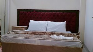 A neatly made bed with a tufted headboard, a bedside table, and a plain wall with a light fixture. - Hotel The Prime (Rawalpindi)
