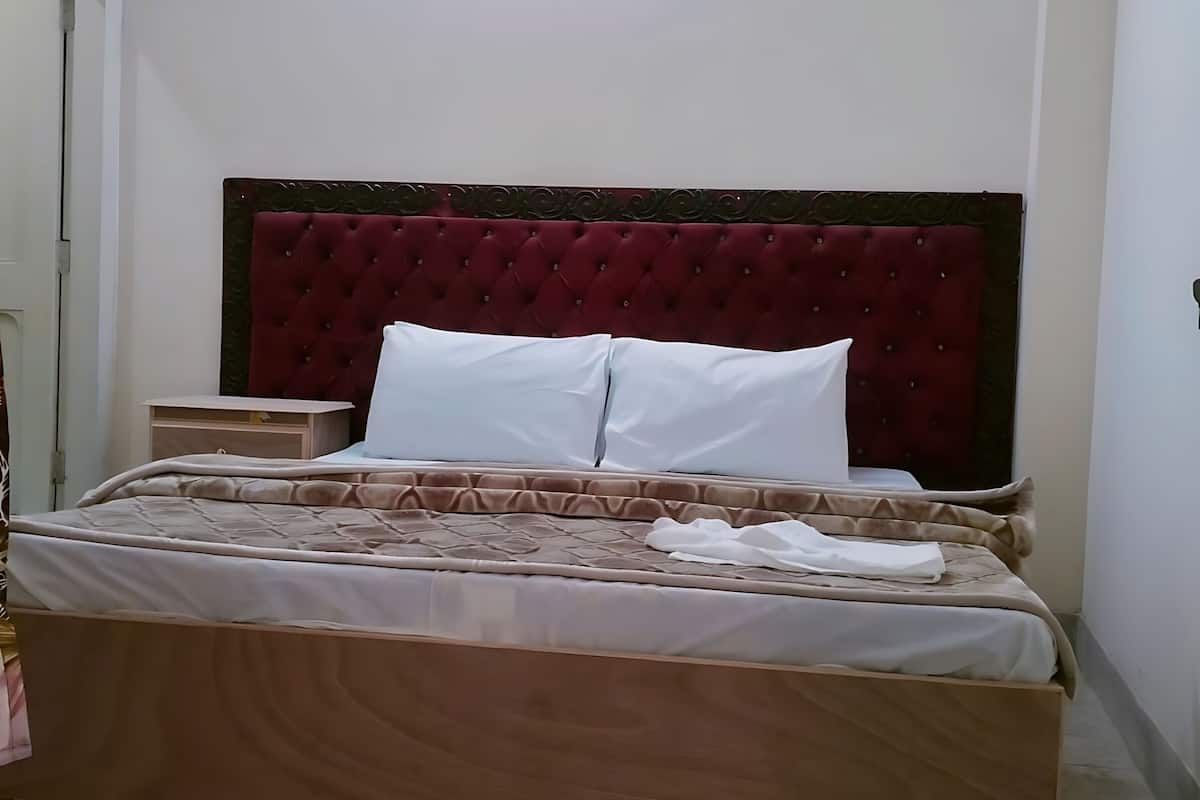Uma cama bem arrumada com cabeceira estofada, mesa de cabeceira e parede lisa com luminária.