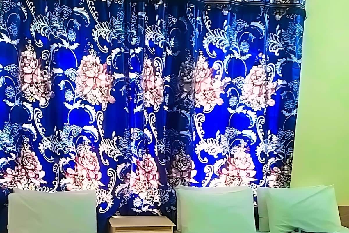 Quarto com duas camas de solteiro, uma pequena mesa de cabeceira e cortina com padrão floral.