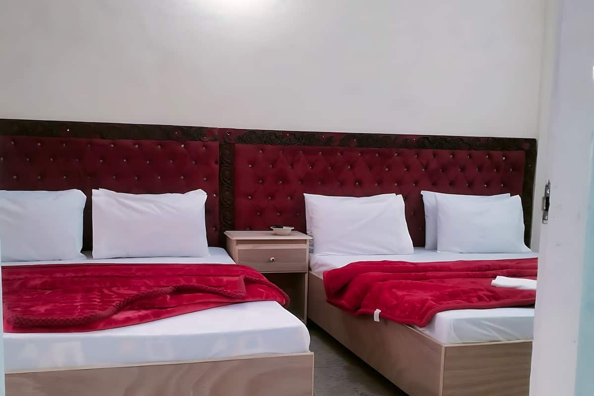 Quarto de hotel com duas camas, cada uma com um cobertor vermelho, uma cabeceira de madeira e uma pequena mesa de cabeceira com abajur.