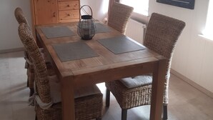 Un área de comedor con una mesa de madera, sillas de mimbre, un televisor sobre un mueble de madera y un cuadro enmarcado en la pared.