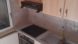 Una cocina con armarios de madera clara, estufa negra, un lavamanos y un ventanal.
