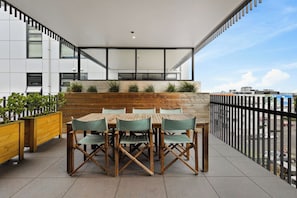 An outdoor terrace with a wooden table and chairs, a wooden bench, and a railing. - Premium Property with Large Balcony by Zodiak (Mount Eden)
