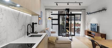 Une cuisine moderne dotée d’une cuisinière intégrée, d’un évier et d’un pare-feu en marbre. On y trouve également un coin repas avec une table et des chaises en bois, ainsi qu’un canapé.