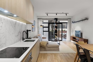 A modern kitchen with a built-in stove, a sink, and a marble backsplash. There is a dining area with a wooden table and chairs, and a sofa. - Premium Property with Large Balcony by Zodiak (Mount Eden)
