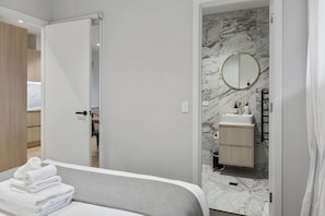 A hotel room with a bed, a bathroom with a marble wall, and a wooden wardrobe. - Premium Property with Large Balcony by Zodiak (Mount Eden)