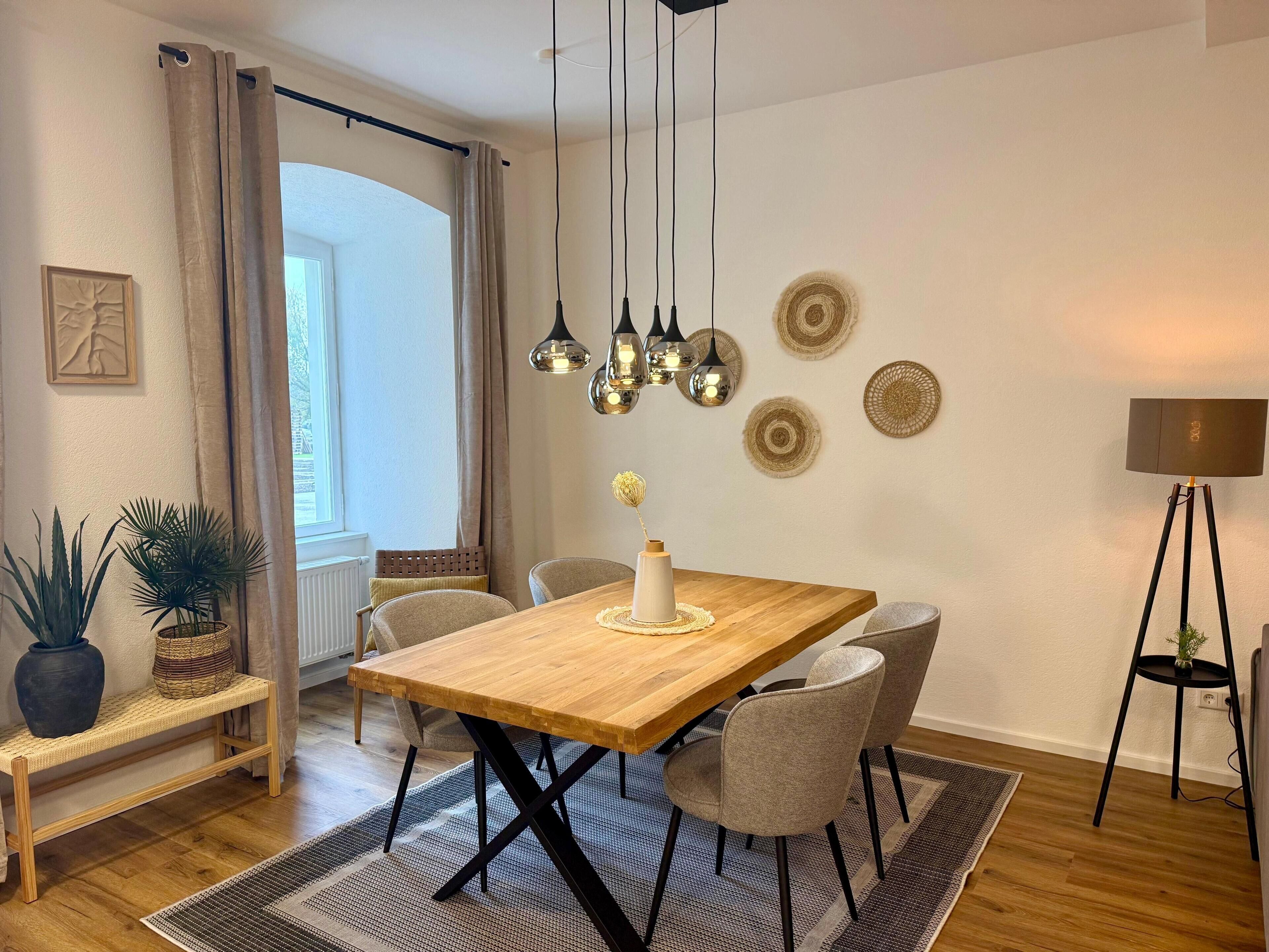 A dining area with a wooden table, four chairs, a bench, and a potted plant.